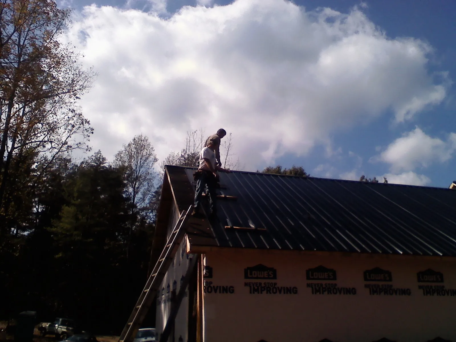 Roofer fastening dark metal panels high against a cloudy sky, from a Roof Inspection job in Lakeville
